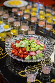 Crudities, cherry tomatoes and cut pieces of fresh melon and watermelon as cocktail snacks on a buffett table with drinks