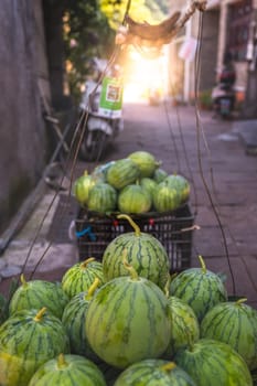 Huge watermelons for sale packed and piled in a plastic boxes to be taken by a porter to the local fruit and vegetable market, Feng Huang town, China