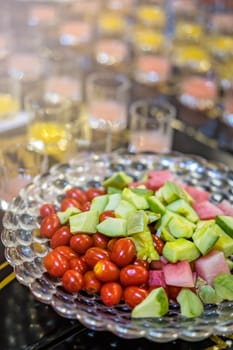 Crudities, cherry tomatoes and cut pieces of fresh melon and watermelon as cocktail snacks on a buffett table with drinks