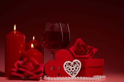 Gift boxes, two glasses with wine, burning candles, red roses and hearts on red background. Valentine's day. Wedding day.  Design element for romantic greeting card and invitation.