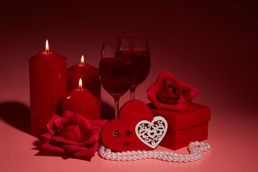 Gift boxes, two glasses with wine, burning candles, red roses and hearts on red background. Valentine's day. Wedding day.  Design element for romantic greeting card and invitation.
