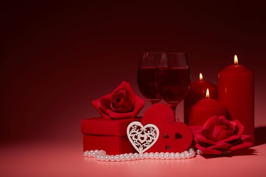 Gift boxes, two glasses with wine, burning candles, red roses and hearts on red background. Valentine's day. Wedding day.  Design element for romantic greeting card and invitation.