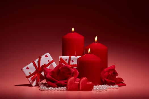 Still life with gift boxes, burning candles, red roses and hearts on red background. Valentine's day. Wedding day. Design element for romantic greeting card and invitation.