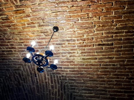 Antique chandelier style with modern lights. It hangs on a red brick ceiling. Rusty look picture.