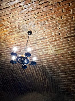 Antique chandelier style with modern lights. It hangs on a red brick ceiling. Rusty look picture.