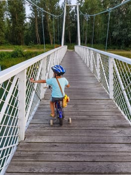 A boy with bicycle on a bridge, touches a bridge. The boy has bicycle helmet. White suspension bridge over the river Drava.