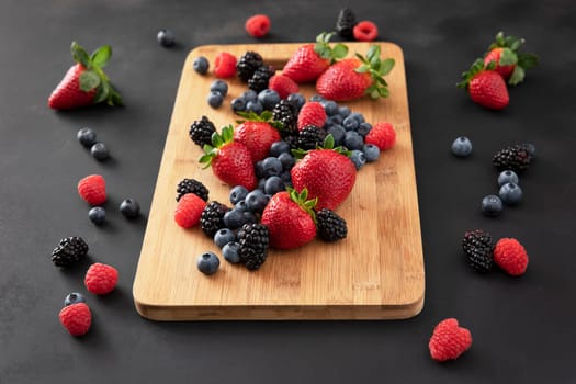 Fresh strawberries, blueberries and blackberries on a wooden cutting board