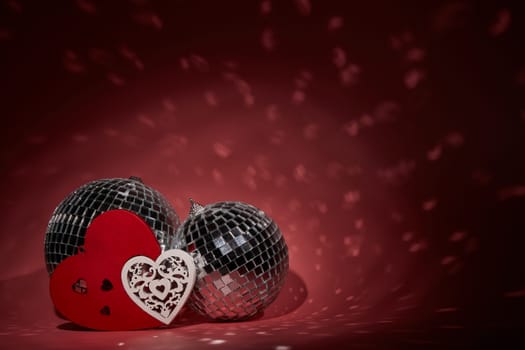 Glittering mirror disco ball  and decorative hearts on dark background with red lighting. Copy space. Valentine's Day background. Holiday party. Nightclub. Entertainment, disco, music show background