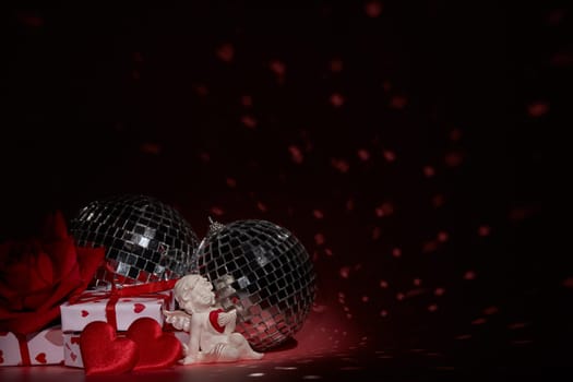 Glittering mirror disco ball  and decorative hearts on dark background with red lighting. Copy space. Valentine's Day background. Holiday party. Nightclub. Entertainment, disco, music show background
