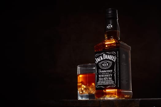 St.Petersburg, Russia - December 2019 - Bottle of Jack Daniel's whiskey and glass with drink and ice  on wooden table on brown background with copy space. Brand of the American whiskey