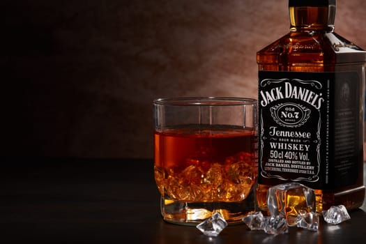 St.Petersburg, Russia - December 2019 - Bottle of Jack Daniel's whiskey and glass with drink and ice  on wooden table on brown background with copy space. Brand of the American whiskey