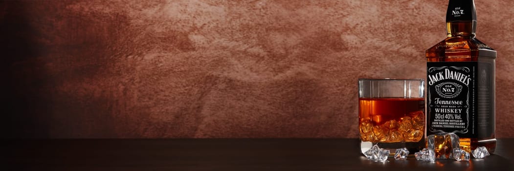St.Petersburg, Russia - December 2019 - Bottle of Jack Daniel's whiskey and glass with drink and ice on wooden table on brown background with copy space. Extra wide panorama banner background