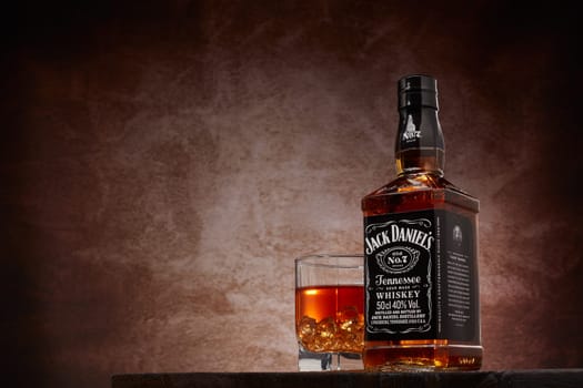 St.Petersburg, Russia - December 2019 - Bottle of Jack Daniel's whiskey and glass with drink and ice  on wooden table on brown background with copy space. Brand of the American whiskey