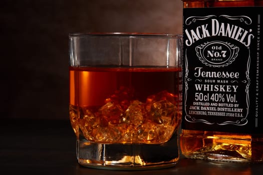 St.Petersburg, Russia - December 2019 - Bottle of Jack Daniel's whiskey and glass with drink and ice  on wooden table on brown background. Brand of the American whiskey