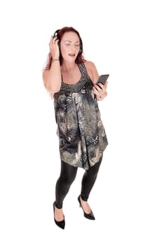 A lovely middle age woman standing in a dress, listening to the.music from her smartphone with head phone isolated for white .background.
