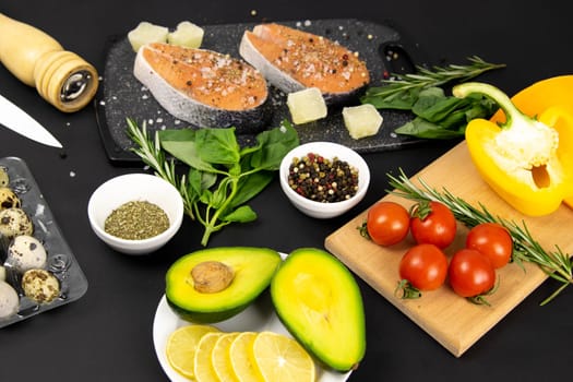 A set of healthy balanced super food, avocado in the foreground, fresh salmon, vegetables, cereals and nuts on a black background. Top view, flat lay