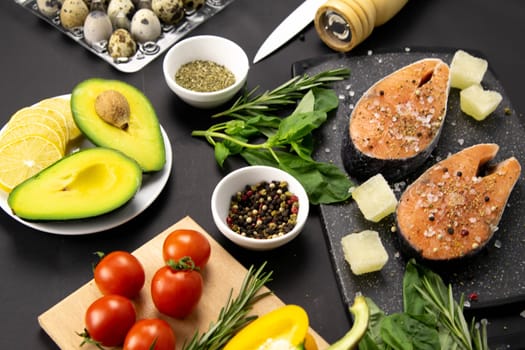 A set of healthy balanced super food, avocado in the foreground, fresh salmon, vegetables, cereals and nuts on a black background. Top view, flat lay