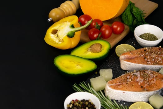 A set of healthy balanced super food, avocado in the foreground, fresh salmon, vegetables, cereals and nuts on a black background. Top view, flat lay