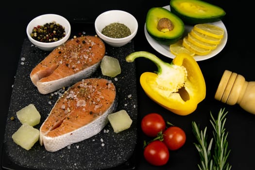 A set of healthy balanced super food, avocado in the foreground, fresh salmon, vegetables, cereals and nuts on a black background. Top view, flat lay