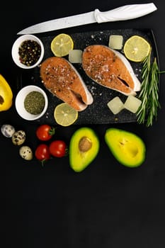 A set of healthy balanced super food, avocado in the foreground, fresh salmon, vegetables, cereals and nuts on a black background. Top view, flat lay