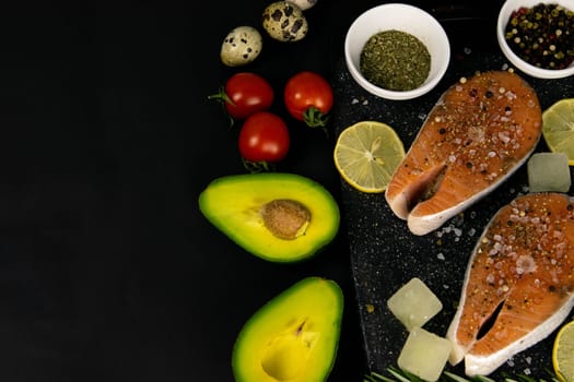 A set of healthy balanced super food, avocado in the foreground, fresh salmon, vegetables, cereals and nuts on a black background. Top view, flat lay