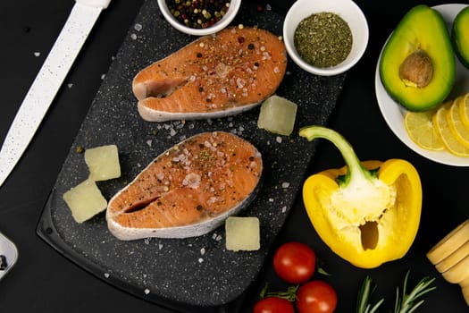 A set of healthy balanced super food, avocado in the foreground, fresh salmon, vegetables, cereals and nuts on a black background. Top view, flat lay