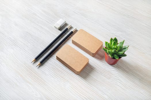 Kraft business cards, pencils, eraser and plant on light wood table background. Blank stationery set. Template for branding identity.
