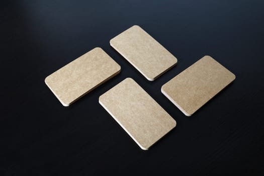 Stacks of blank kraft business cards on black wooden background. Template for branding ID.