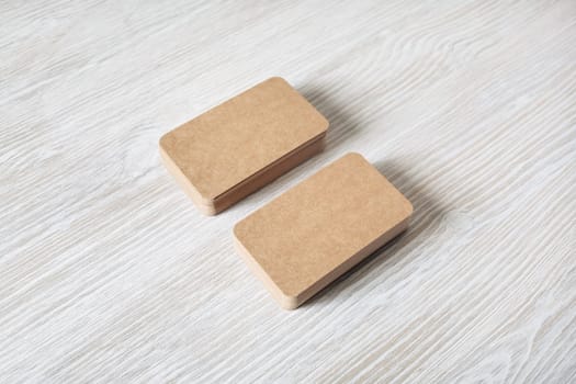 Photo of blank kraft business cards stacks on light wood table background. Template for branding identity.