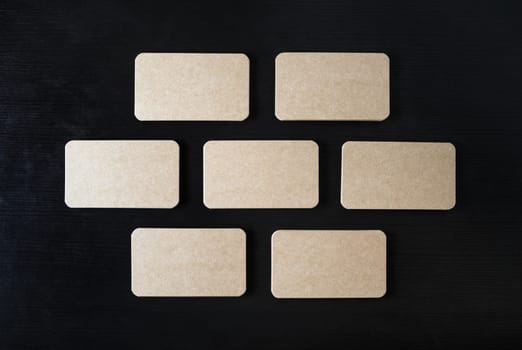 Blank kraft business cards mock-up on black wood table background. Copy space for text. Flat lay.