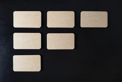 Blank kraft business cards on black wood table background. Template for branding identity. Flat lay.