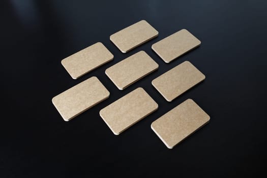 Blank kraft business cards lying in the shape of a heart on black wooden background.