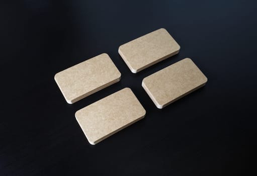 Four piles of blank kraft business cards on black wooden background. Corporate ID template.