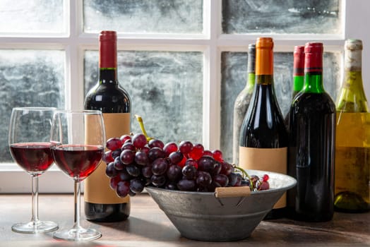 two wineglasses, red and white grapes with bottles of a red wine