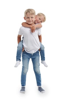 Friendly family. Older brother is holding behind the back younger boy, standing isolated on a white background. Happy siblings. Two little brothers. Concept of people and family