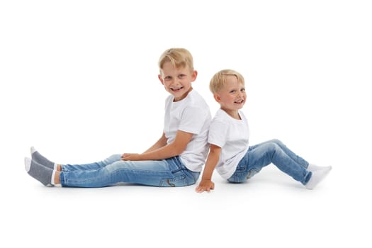 Friendly family. Older brother and younger boy are sitting with backs to each other isolated on a white background. Happy siblings. Two little brothers. Concept of people and family