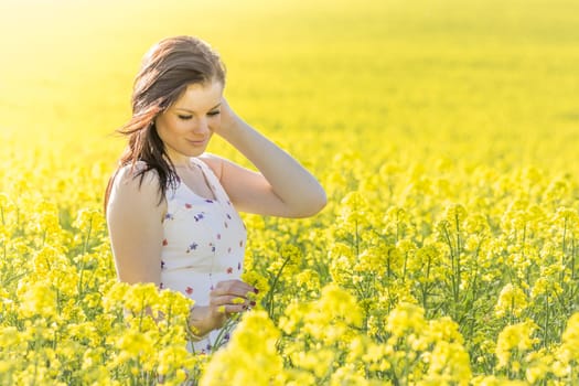 Beautiful girl eyes closed in yellow flowers field infinite horizon. Sunny sun sunshine and authentic lifestyle in windy weather hair.