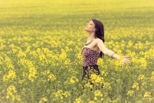 Attractive young beauty girl enjoying the warm sunny sun in nature rapeseed field takes time feeling sustainability and contemplation.