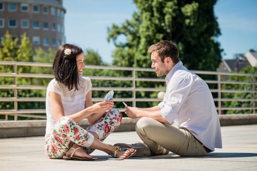 Young couple playing cards outdoor sitting on ground