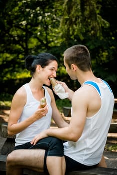 Young couple eating after sport training outdoor in nature - man feeds woman