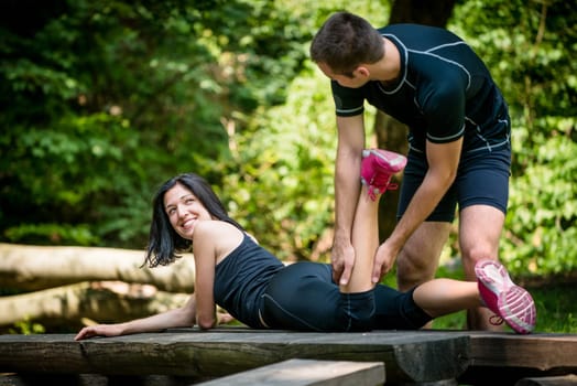 Relax after sport - man massaging calf of his friend outdoor - woman lies on bench
