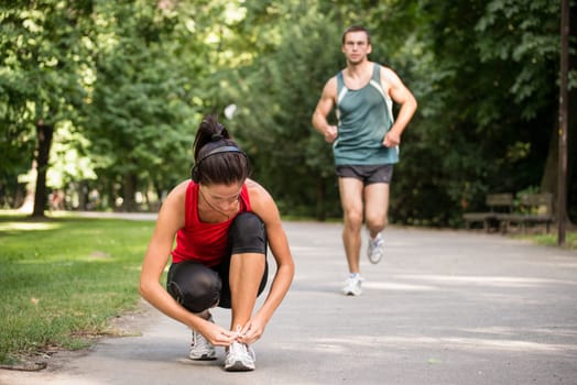 Young sport woman tying shoelace, man in behind is jogging