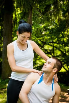 Young woman massaging her friend after sport training in nature