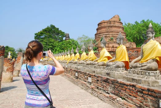 Tourist (young woman) taking picture of siting budha statues in Ayutthaya, Thailand