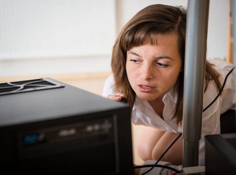 Young business woman trying to repair computer under table
