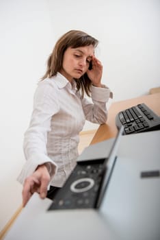 Business person in depression reaching hand and taking paper from printer on workplace