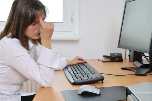 Young tired business woman with headache sitting at computer in workplace holding head