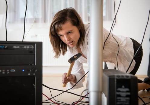 Young business woman having problem with computer and trying to recover it with hammer