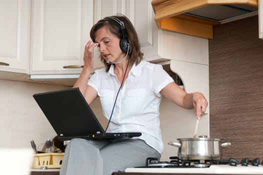 Young business woman having work conference call from home while cooking meal in kitchen