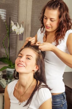 beautiful young woman makes the hairstyle of his girlfriend at home
